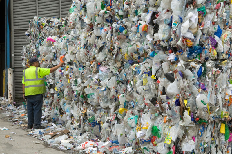 A man stands next to piles of compressed plastic bottles.