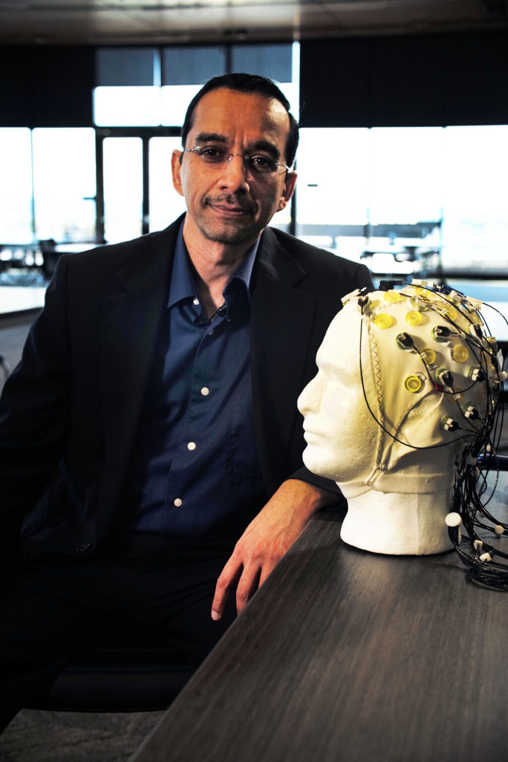 Rajesh Rao sitting next to a plaster head modeling a skull cap brain-computer-interface device