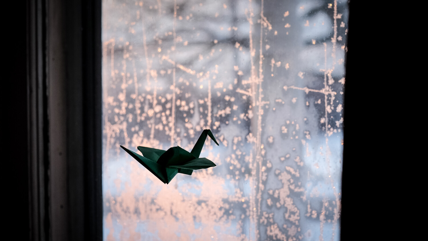 paper crane against a window at sunset