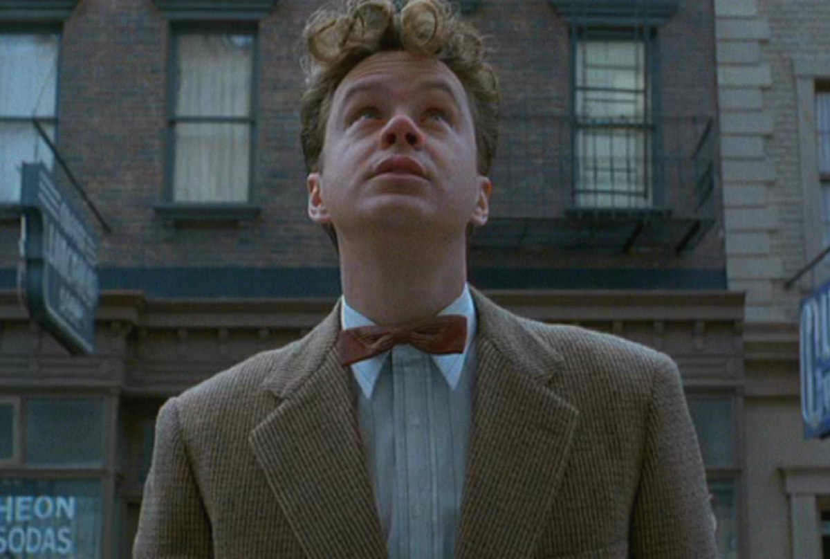 young man in 1950s suit looking up at a tall building